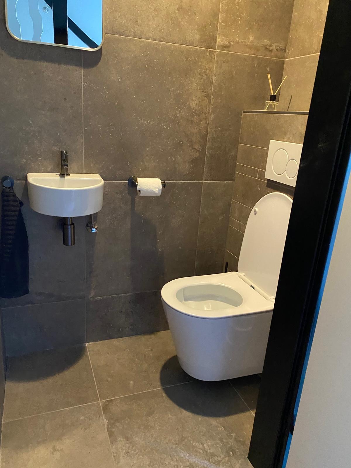 Afgewerkte toiletruimte met hangend toilet en natuurstenen tegels